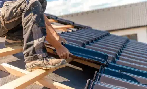 Couvreur installant des tuiles bleues sur une charpente en bois lors d'une rénovation de toiture.