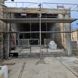 Chantier avec échafaudage Altrad, murs en parpaings et structure en béton en cours de rénovation.