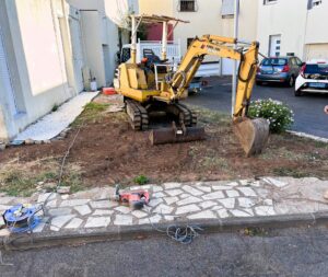 Excavatrice jaune Ammann Yanmar en chantier avec marteau-piqueur et câble sur un terrain résidentiel.