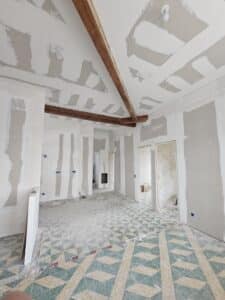 Rénovation intérieure avec plaques de plâtre jointoyées, poutres bois et sol ancien en carreaux de ciment géométriques.