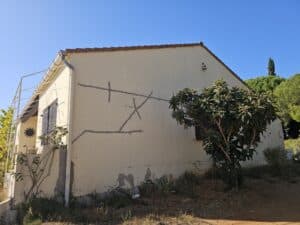 Mur de maison beige avec fissures colmatées de gris sous un ciel bleu.
