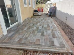Terrasse en carrelage imitation bois gris et marron devant une porte coulissante, chantier extérieur.